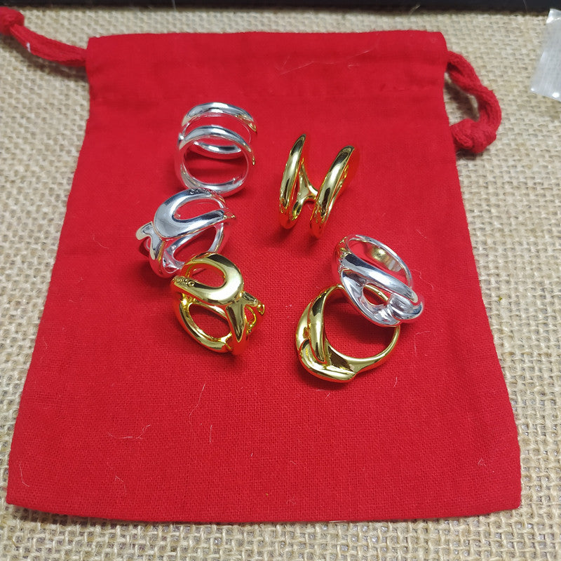 Six twisted metal rings in both silver and gold finishes arranged on a red drawstring pouch over a beige woven mat background.