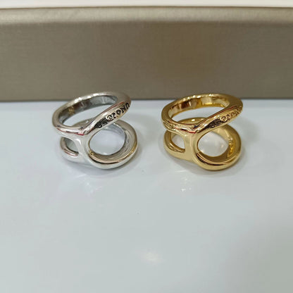 Two abstract open-link rings, one in polished silver and one in polished yellow gold, displayed side-by-side on a white surface with a beige background.