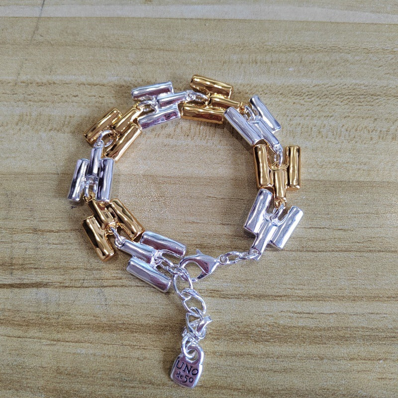 A two-tone metal bracelet with cylindrical links in silver and rose gold, featuring a small hanging padlock charm engraved with 'LOVE', displayed on a light wood grain surface.