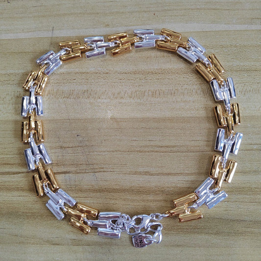 A two-tone metal link bracelet with alternating silver and rose gold cylindrical links, displayed on a light wood grain surface.