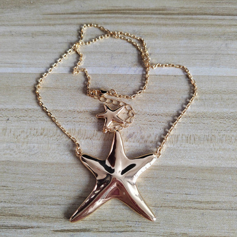 A rose gold starfish pendant necklace with a matching starfish charm on a delicate chain, displayed on a light wood background.