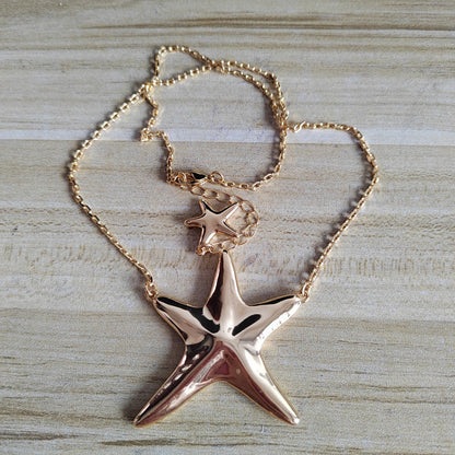 A rose gold starfish pendant necklace with a matching starfish charm on a delicate chain, displayed on a light wood background.