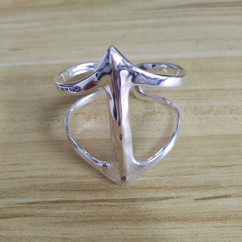 A polished silver ring with a sculptural, abstract design resembling a stylized figure or star, photographed on a light wood grain surface.