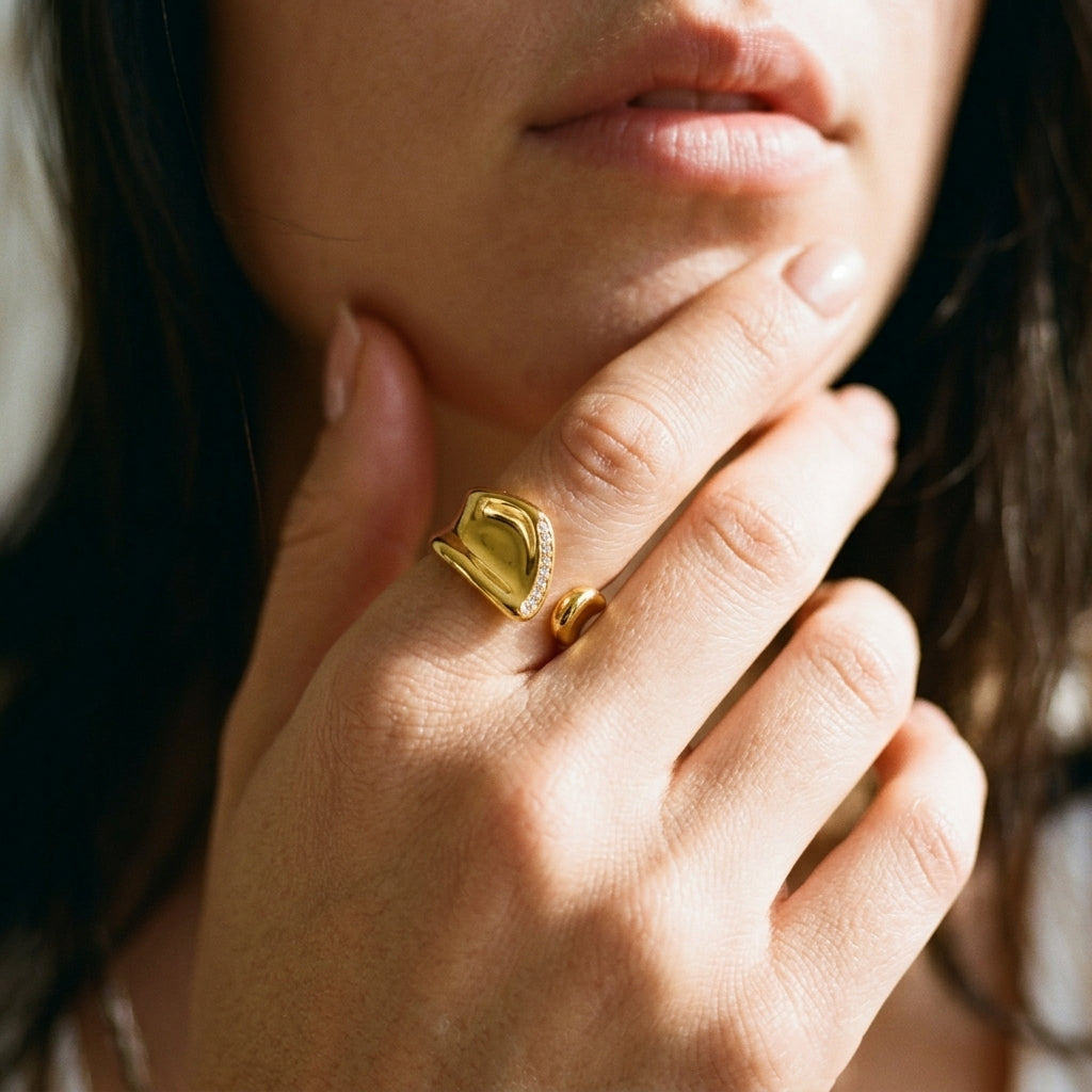 A close-up lifestyle shot of a model wearing a textured gold signet ring with a small halo of clear stones, alongside a slim gold band.