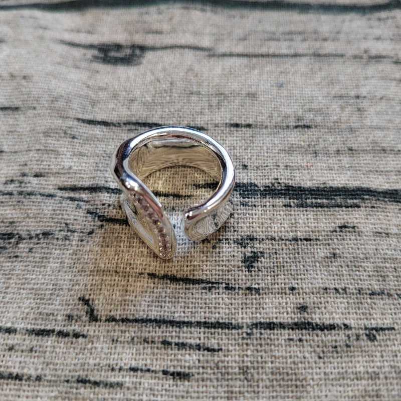 A polished silver open band ring with a textured, hammered finish, resting on a rustic beige linen fabric background.