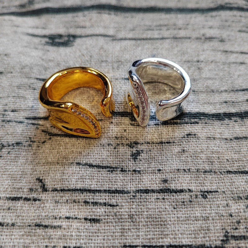 Two leaf-shaped open stretch rings, one in polished yellow gold and the other in polished silver, displayed on a textured gray linen fabric background.