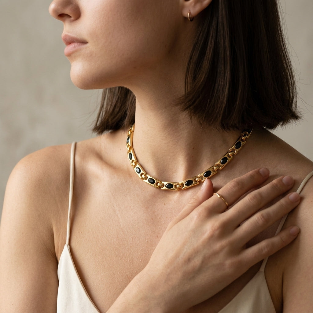 A close-up lifestyle shot of a woman wearing a gold chain necklace with alternating black and gold oval links, paired with a matching gold ring.