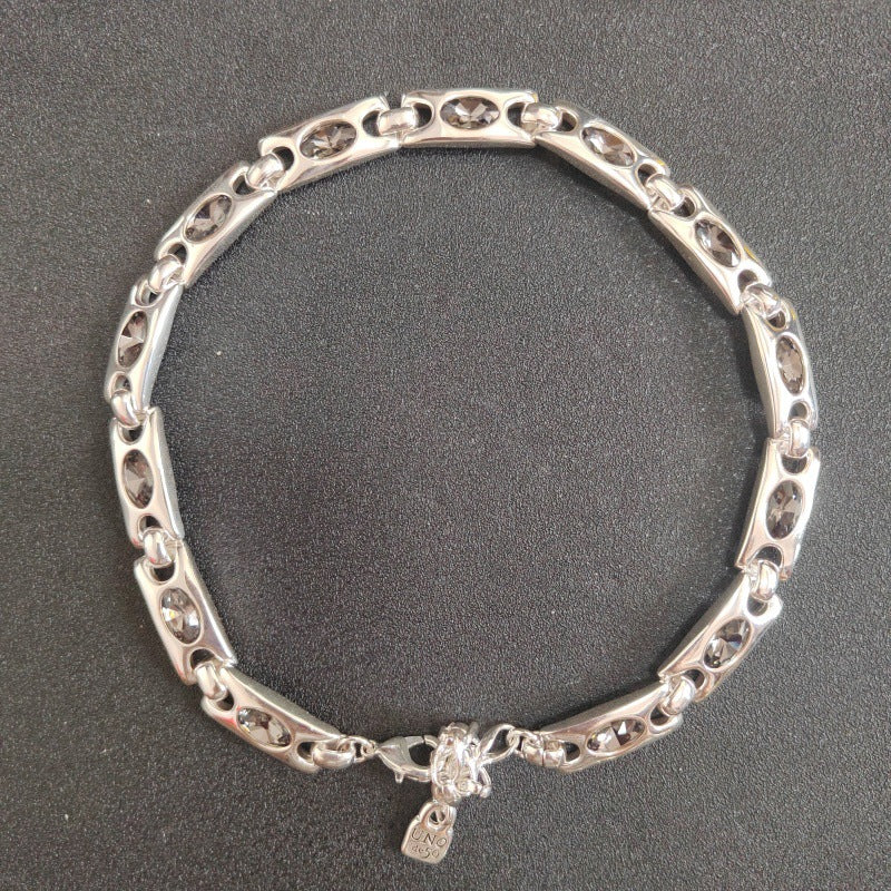 A silver-toned metal link bracelet with a small hanging tag, photographed on a dark textured background.