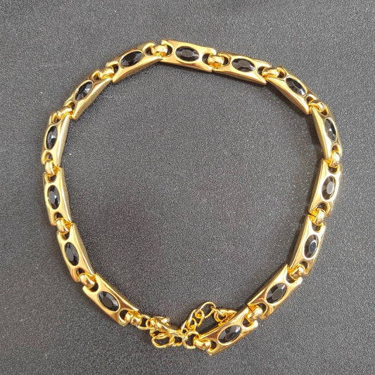 A gold-tone chain bracelet with oval dark inlays, photographed on a dark gray textured background.
