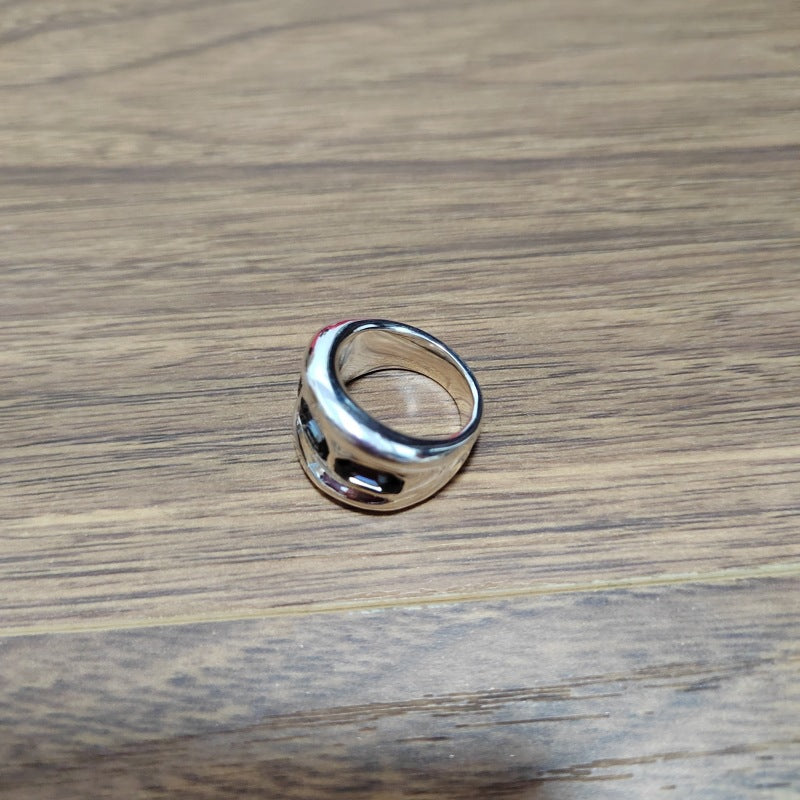 A polished silver ring with a unique curved, wave-like band design, resting on a brown wood-grain surface.