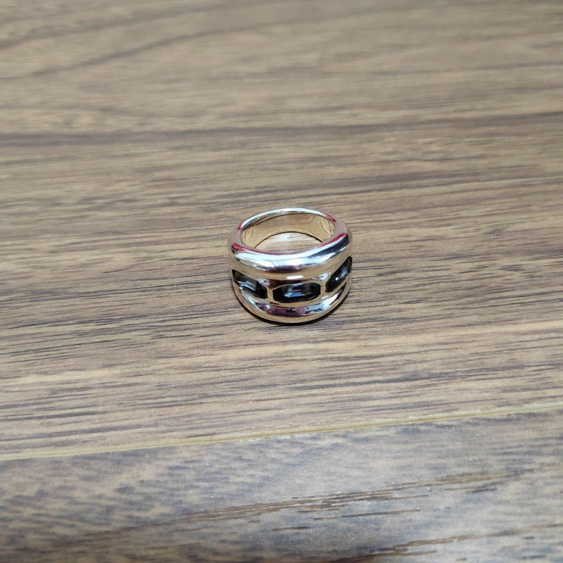 A polished silver ring with a unique geometric, interlocking circular design, resting on a brown wooden surface.