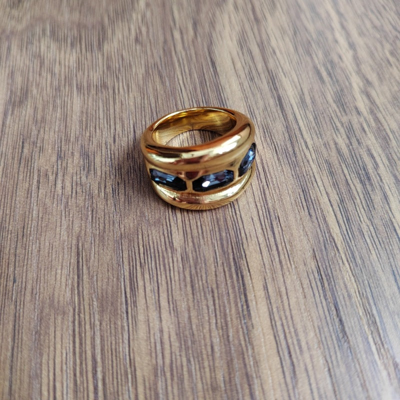 A gold band ring with three dark blue oval inlays, resting on a brown wood-grain surface.