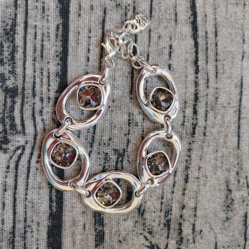 A silver-toned link bracelet featuring oval links and square bezel-set brown gemstones, displayed on a textured gray fabric background.