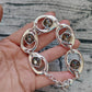 A sterling silver link bracelet with oval links and square smoky brown gemstones, held in a person's hand against a gray wood-textured background.