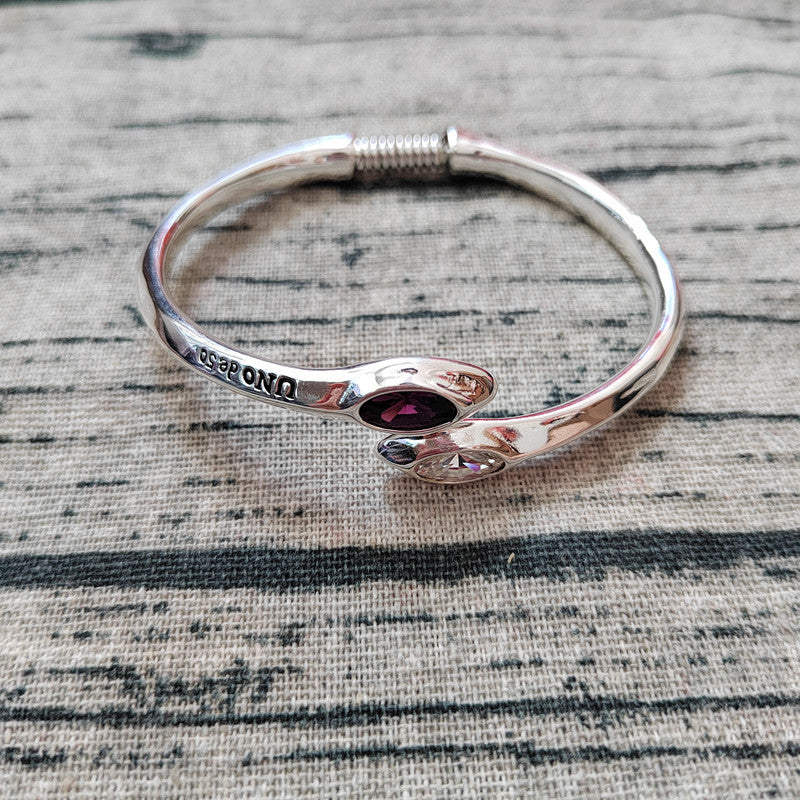 A polished silver bangle bracelet with a butterfly design, featuring a dark red oval gemstone in the center and the brand name 'DIPENDO' engraved on one side, resting on a textured gray fabric background.