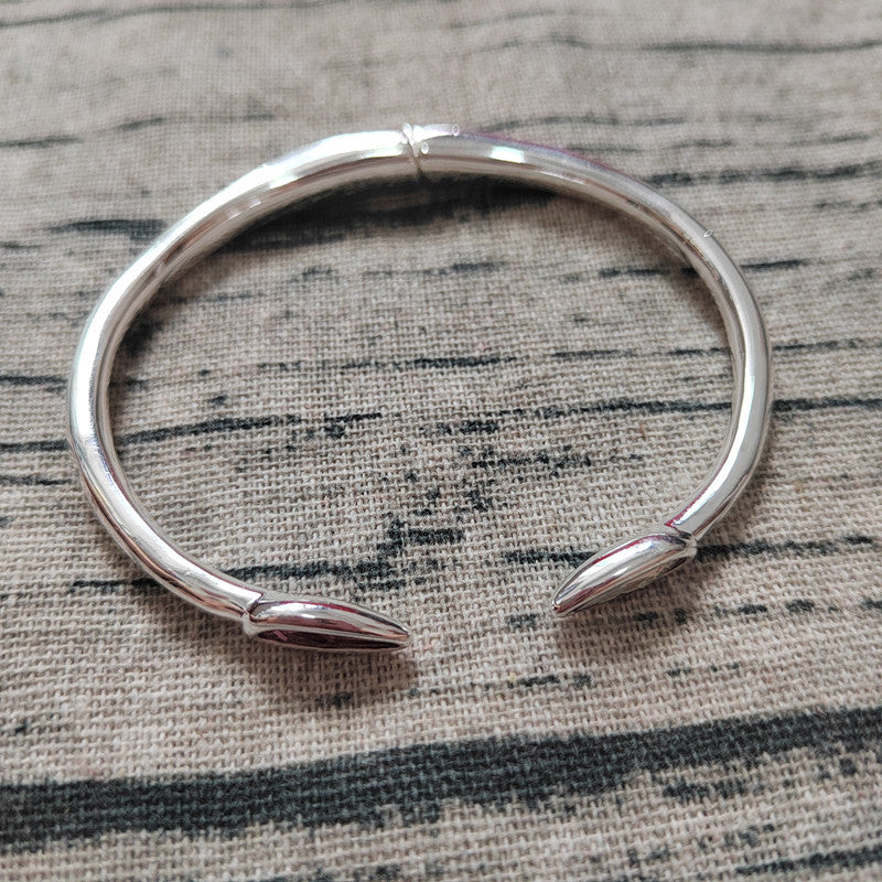 A polished silver-toned open cuff bracelet with pointed ends, photographed on a textured woven fabric background.