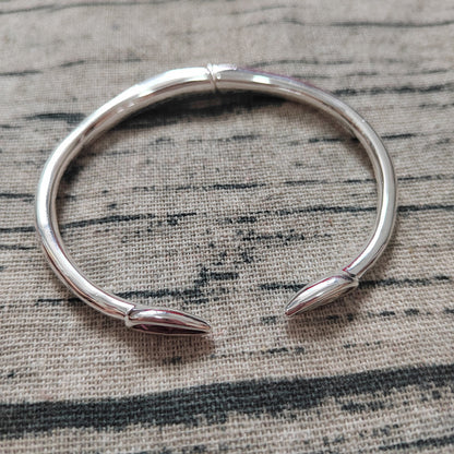 A polished silver-toned open cuff bracelet with pointed ends, photographed on a textured woven fabric background.