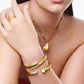 A close-up lifestyle shot of a model wearing a gold jewelry set, featuring a heart-shaped pendant necklace, a multi-band cuff bracelet, and a ring on her finger.