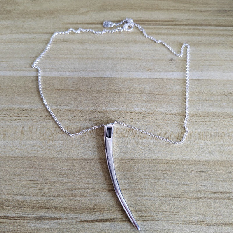 A silver-toned necklace with a curved, hook-like pendant resting on a light wood grain surface.