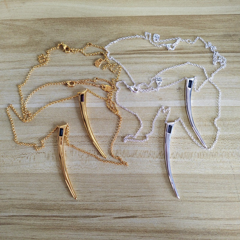 Two curved necklace pendants with chain straps, one in gold-toned metal and one in silver-toned metal, displayed on a light wood surface.