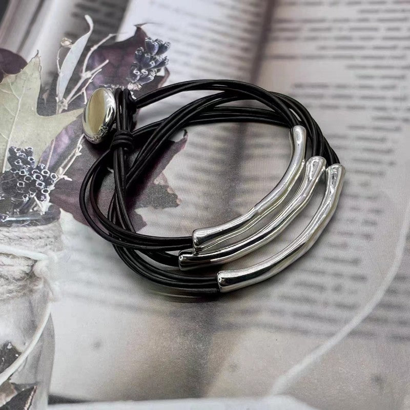 A stack of black cord bracelets with polished silver-toned curved bar elements and a small oval cream stone, arranged on an open book.