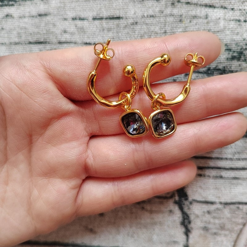 Gold hoop earrings with gemstones held in a hand against a neutral background