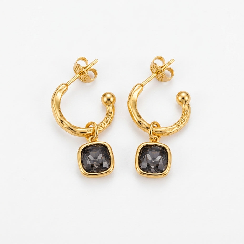 A pair of gold huggie hoop earrings with a small gold bead and a square dark gray gemstone dangle, shown on a clean white background.