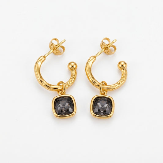A pair of gold huggie hoop earrings with a small gold bead and a square dark gray gemstone dangle, shown on a clean white background.
