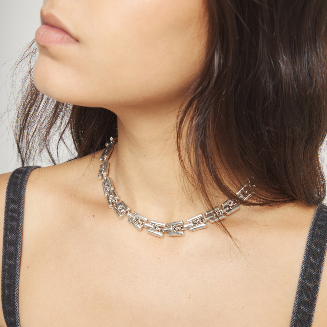 Close-up of a person wearing a silver chain necklace with a neutral background