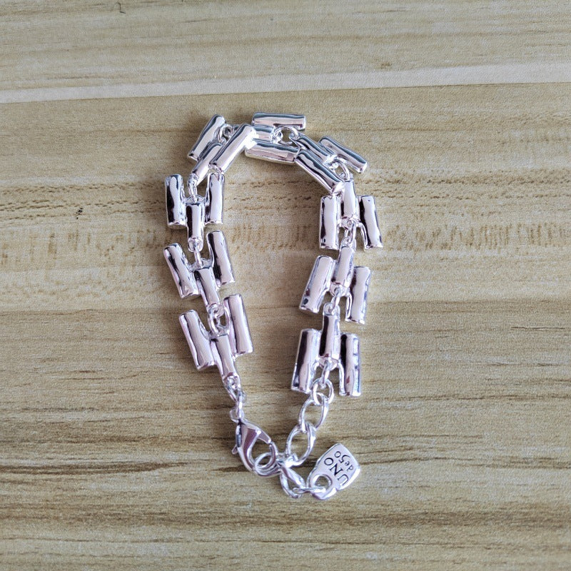 A silver-toned link bracelet with a unique segmented, cylindrical chain design and a small charm, displayed on a light wood background.