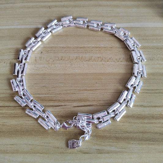 A silver-toned link bracelet with a textured, segmented design, displayed on a light wood grain surface.