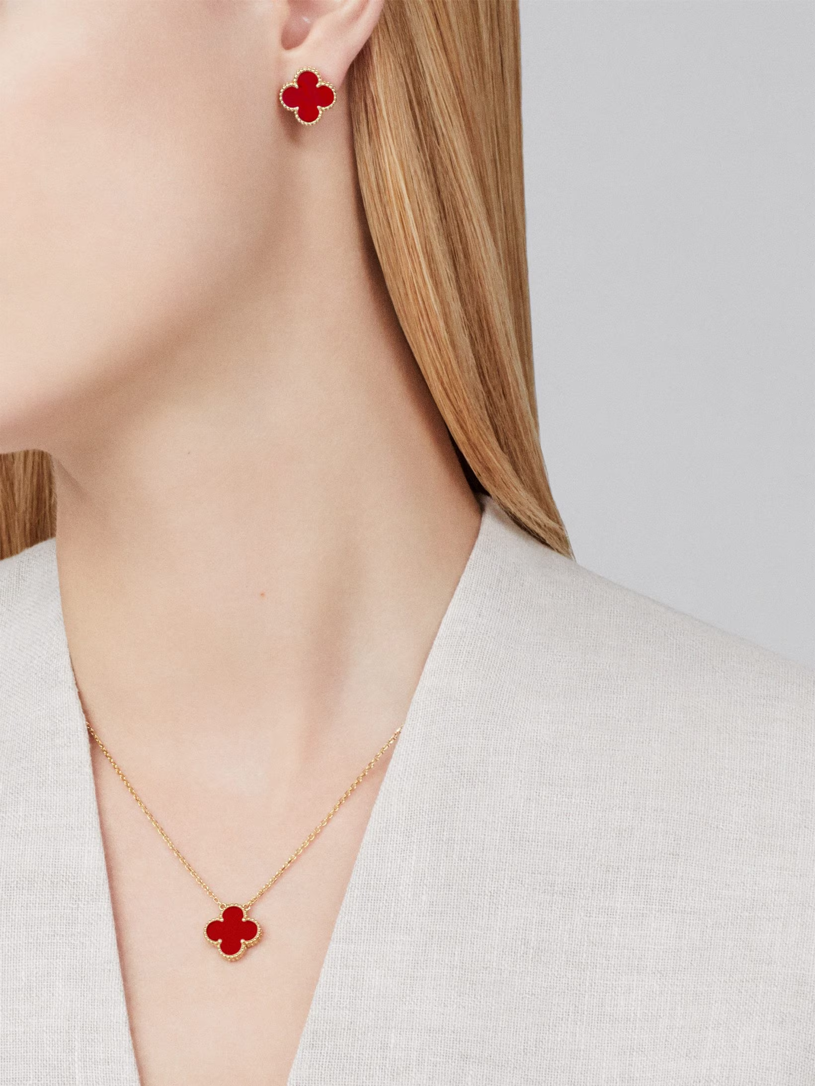 Red clover-shaped earrings and necklace on a model against a neutral background