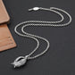 Silver chain necklace with a leaf pendant on a dark surface