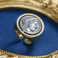 Gold ring with a silver coin featuring a face design on a blue fabric background