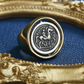 Gold ring with a silver emblem on a blue fabric background