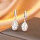 Pearl earrings with silver teardrop designs on a soft fabric background