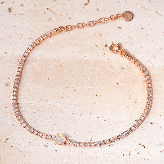 Rose gold bracelet with clear stones on a beige textured background