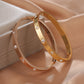 Gold hoop earrings with embedded stones on a beige fabric background
