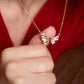 Gold bow-shaped necklace held by a hand against a red background