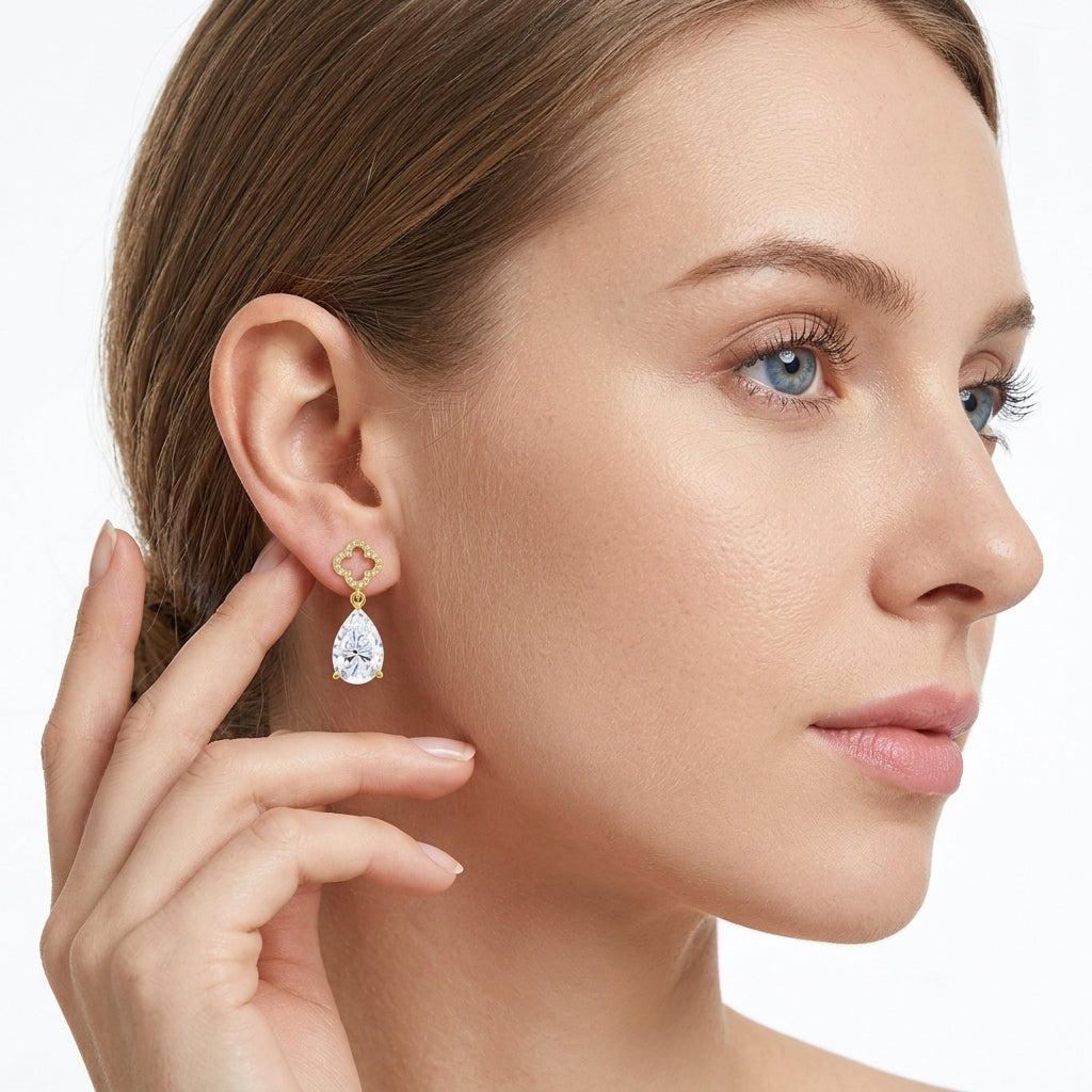 Model wearing gold asymmetric moissanite drop earrings with heart and pear drops.