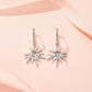Celestial starburst crescent moon moissanite dangle hoop earrings resting on pink silk.