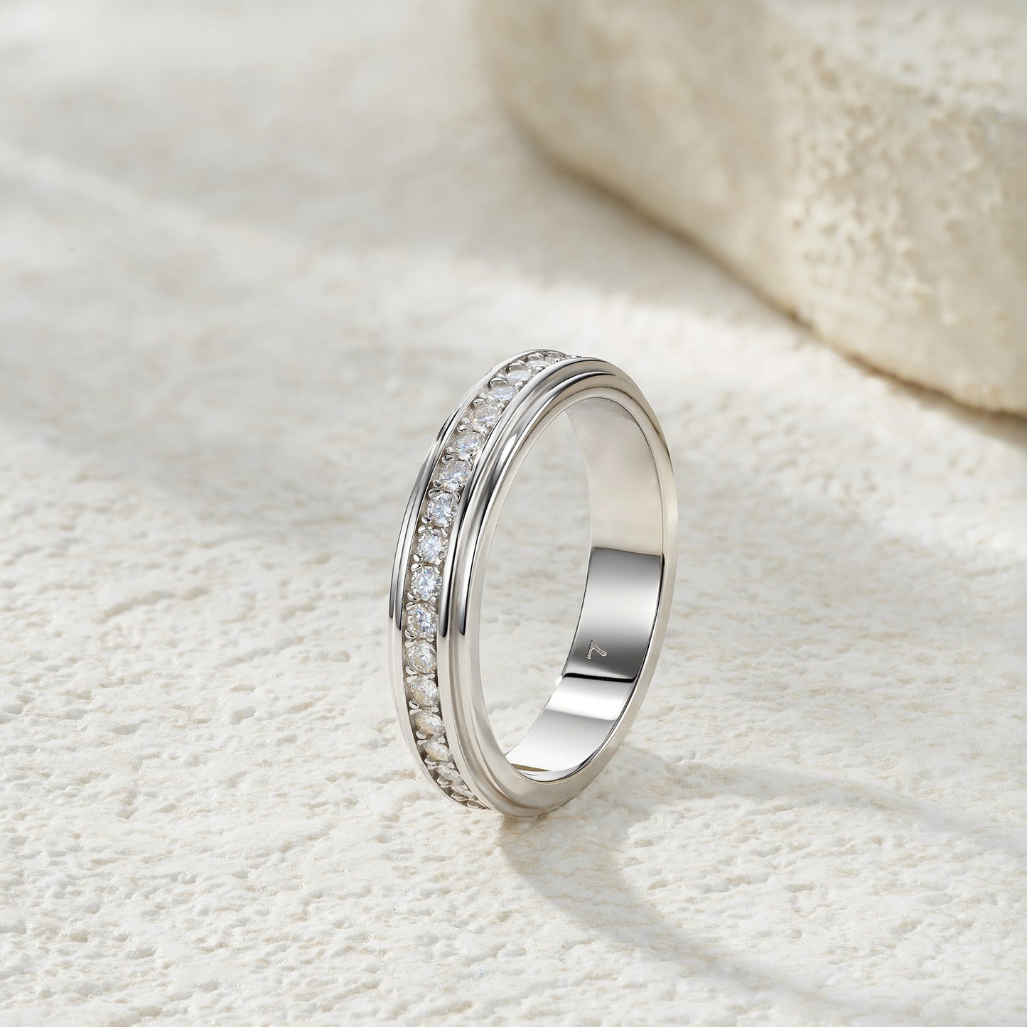 Side profile view of beveled edge channel set moissanite eternity stacking ring on textured stone.