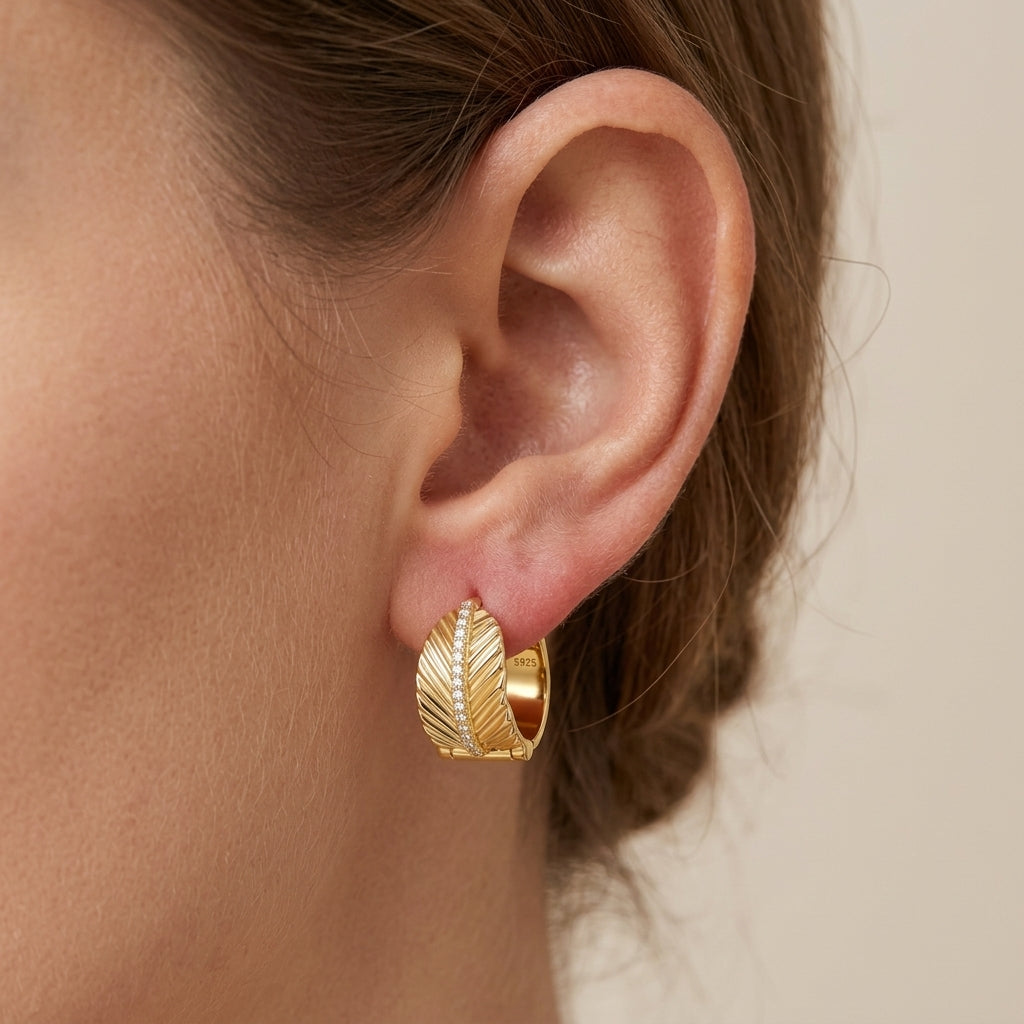 Side profile view of a model wearing gold leaf textured chunky huggie earrings.