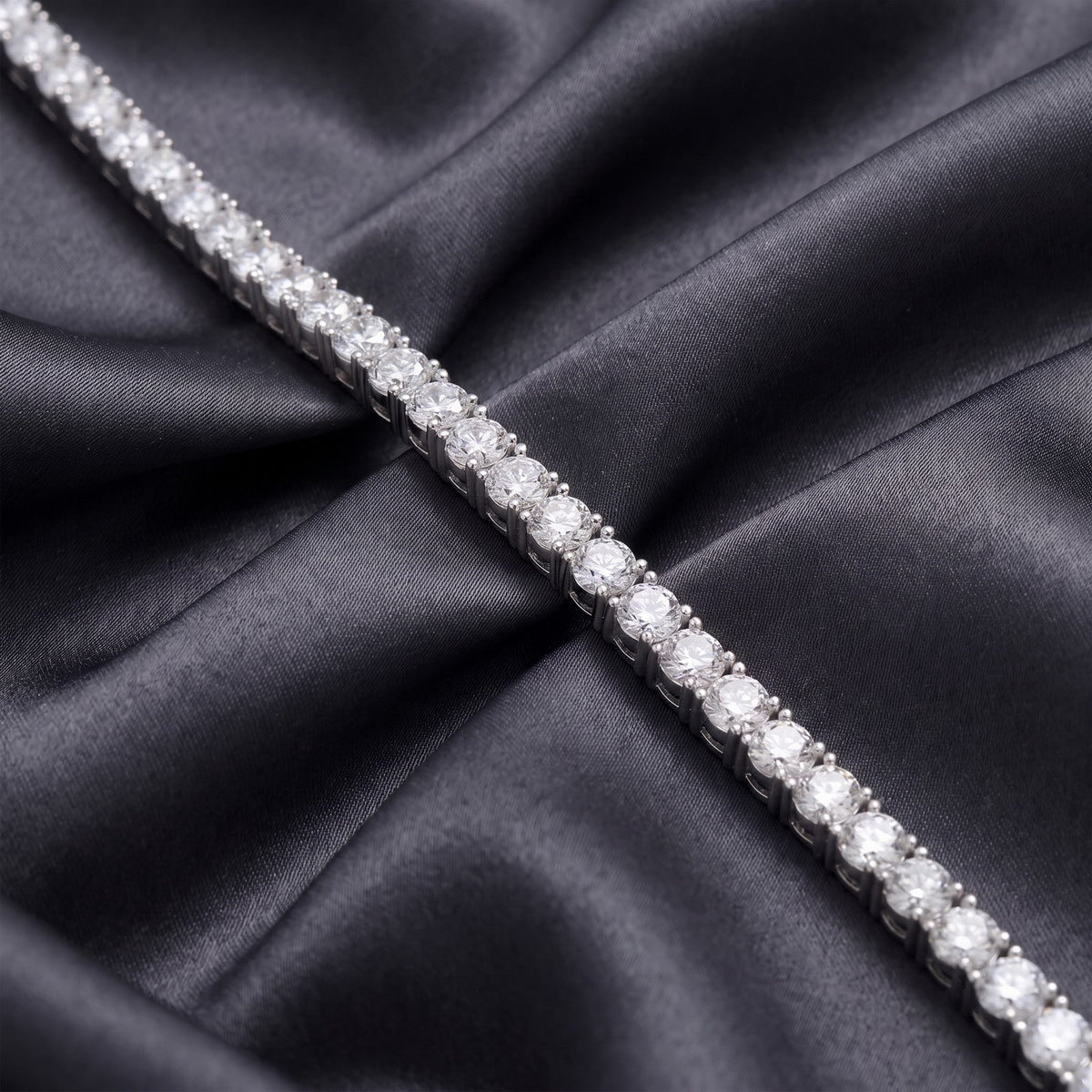 Straight profile view of classic 4-prong round lab-grown diamond tennis bracelet on dark silk.