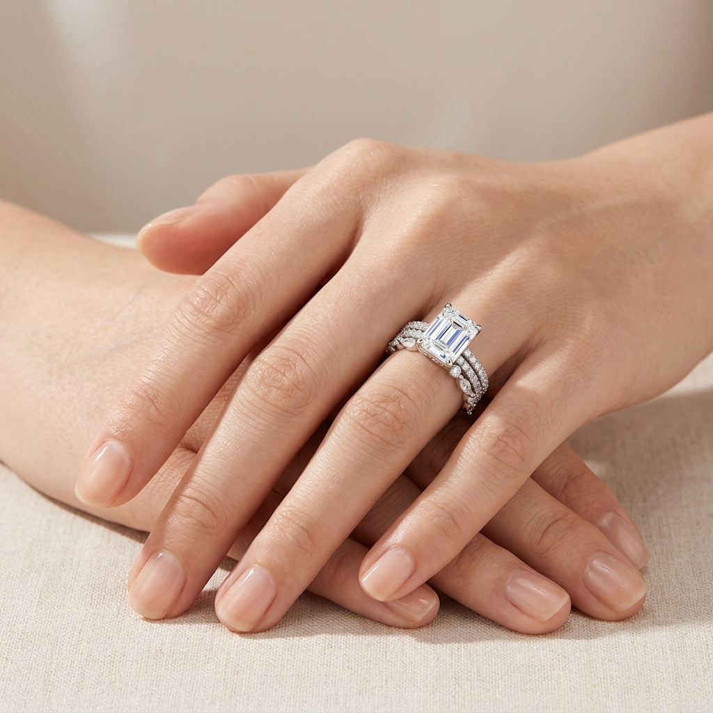 High-end fashion lookbook view of a model's hand gracefully displaying a classic emerald cut moissanite 3 piece bridal stacking ring set.