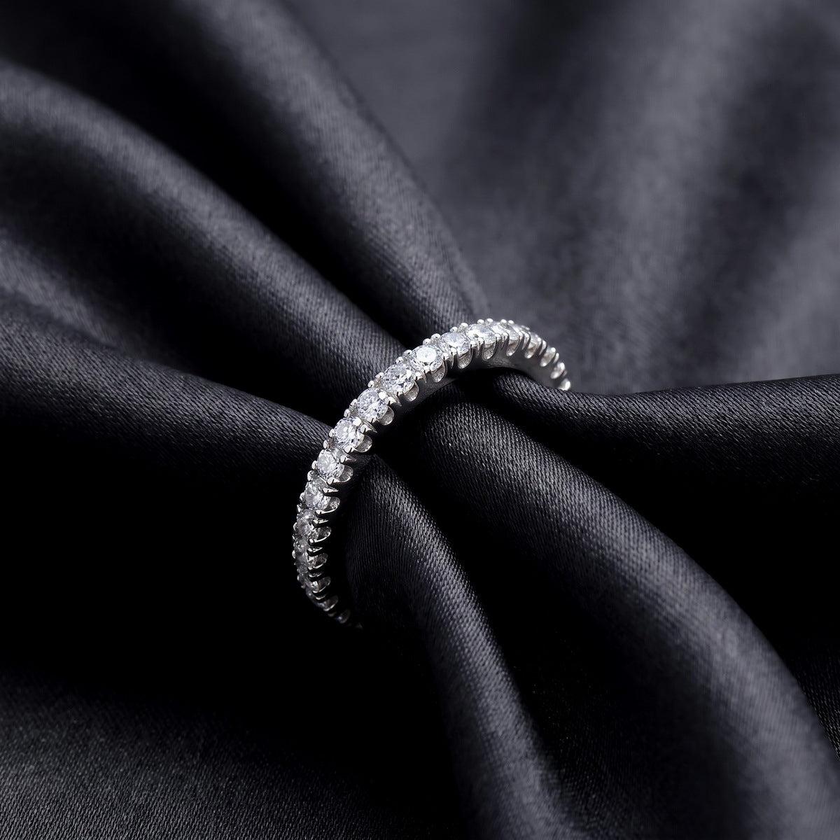 Close up side view of lab grown diamond eternity band ring on black silk