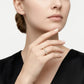 A close-up of a woman wearing a delicate gold ring with small clear stones on her finger, set against a clean light gray background.