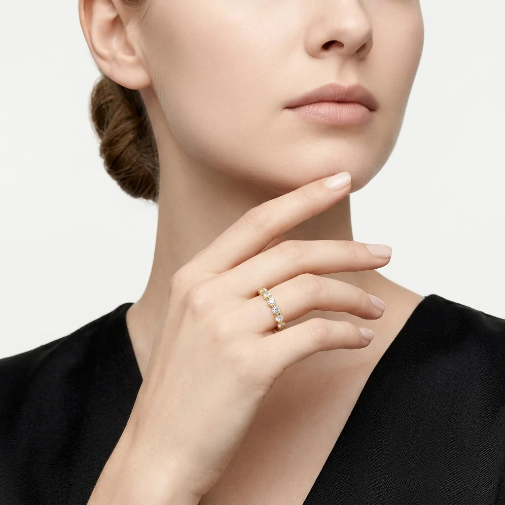 A close-up of a woman wearing a delicate gold ring with small clear stones on her finger, set against a clean light gray background.