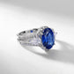Three-quarter studio product view of a classic oval-cut blue sapphire halo ring casting a crisp gradient shadow.