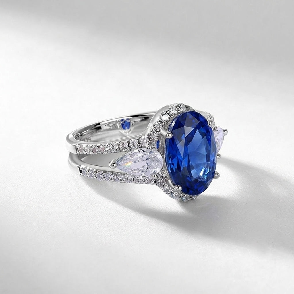 Three-quarter studio product view of a classic oval-cut blue sapphire halo ring casting a crisp gradient shadow.